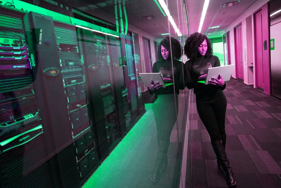 Femme sur un ordinateur portable dans un datacenter aux serveurs en miroir.